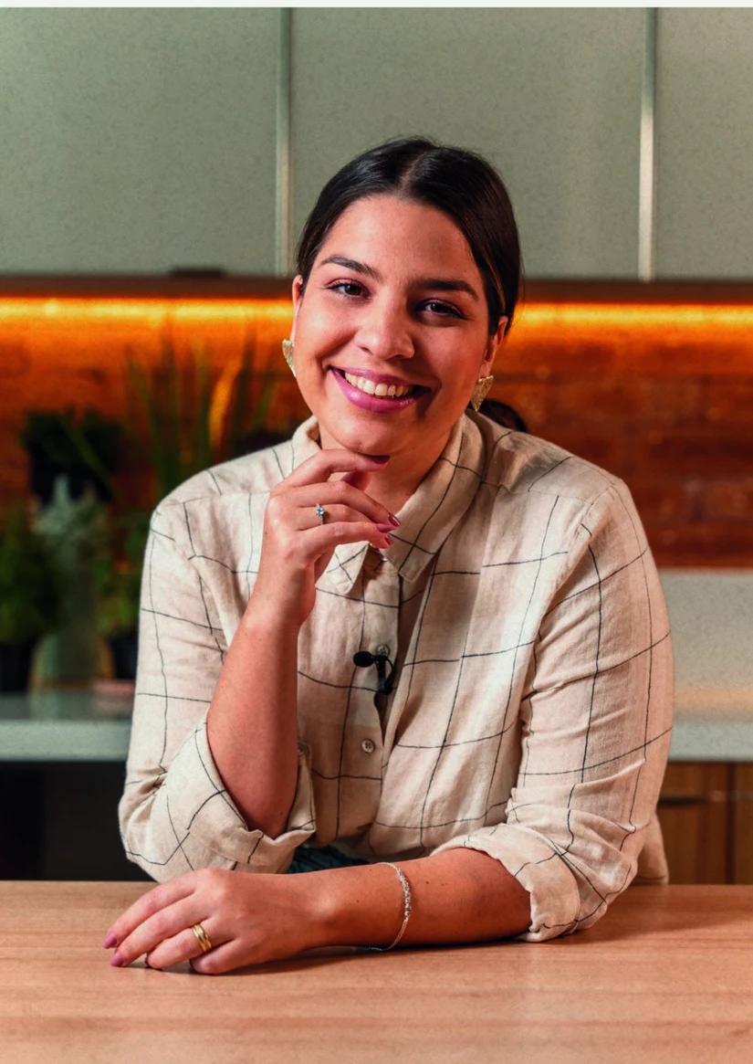 Bruna Hermogenes sentada à mesa, sorrindo